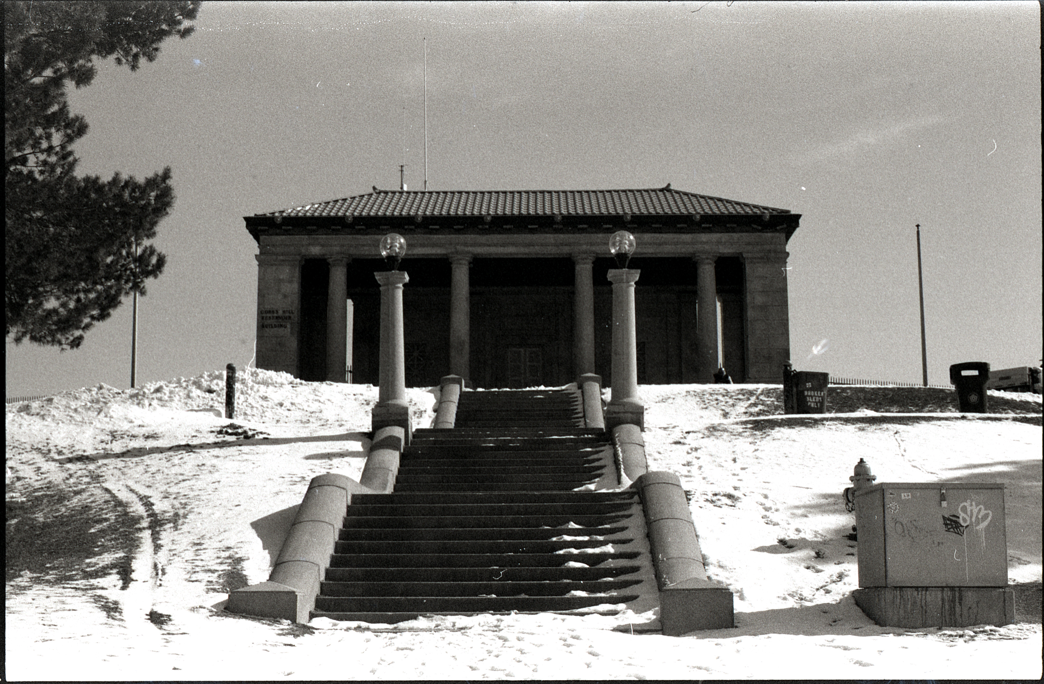 photo, black and white with some film artifacting: stairs leading up through snow towards a building with imposing columns